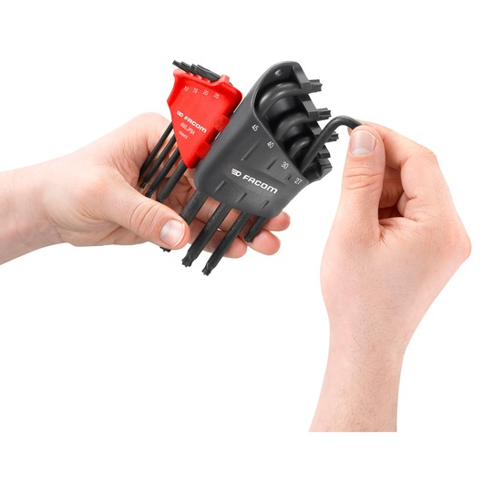 Two hands are holding and selecting hex keys from a Facom hex key set, with black and red holders marked with sizes.