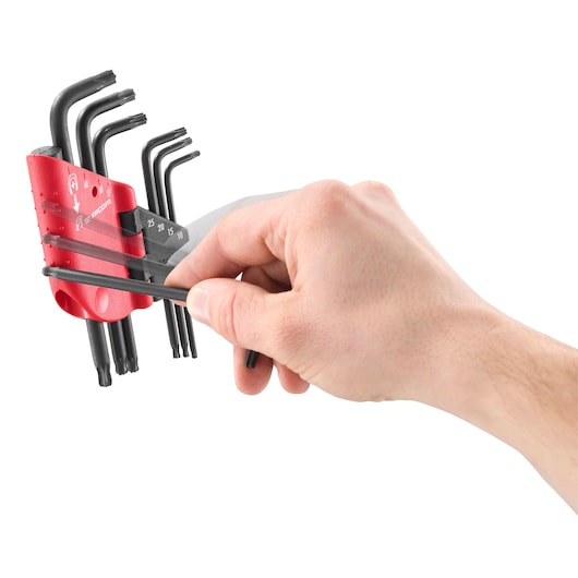 A hand is selecting a black hex key from a Facom branded red holder containing a set of various sized hex keys.