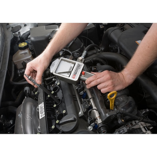 Facom 912 automotive diagnostic tool in use on car engine, close-up showing hands operating the device.