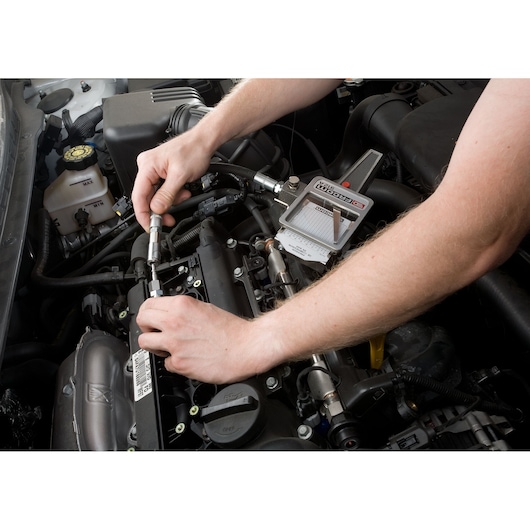 Facom 912 fuel injection pressure tester on car engine in use, close-up of hands connecting tool.