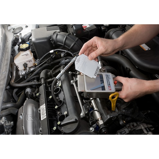 Facom 912 automotive diagnostic tool used on a car engine, close-up view of hands operating the device.