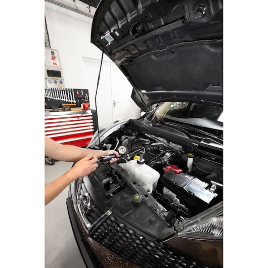 Photo of Facom 920B tool used on a car engine in a workshop with the hood open.