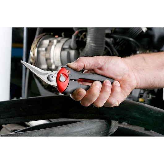 Facom 980C aviation snips with black and red handle shown in a hand during use near machinery.