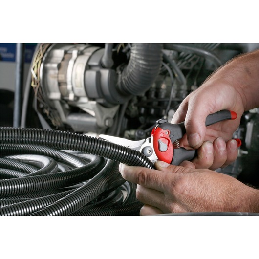 Facom 980C cable cutter with red and black handle cutting black corrugated tubing near engine