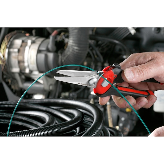 Facom 980 scissors with red and black handles cutting green wire in an automotive environment.