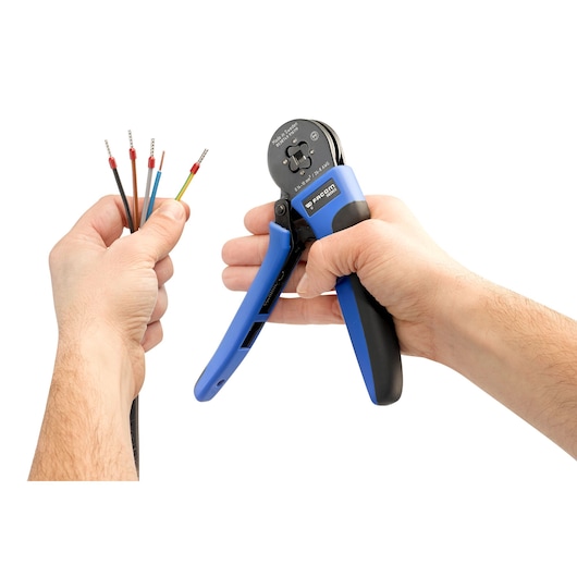 Photo of Facom 985905 wire crimping tool with blue and black handles, held in hand near insulated wires, front angle.