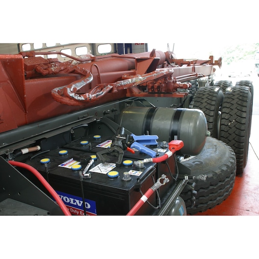Facom 985913 photography showing heavy-duty truck battery setup with cables and tools near tires.