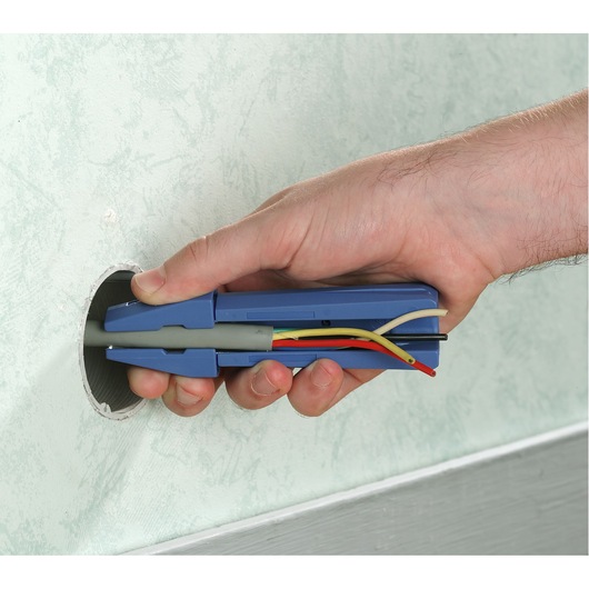 Facom 985962 wire stripper tool held by hand, stripping colored electrical wires near wall opening.