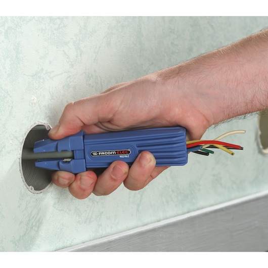 Facom wire installer tool 985962 held in hand, blue plastic handle, guiding wires through wall opening.