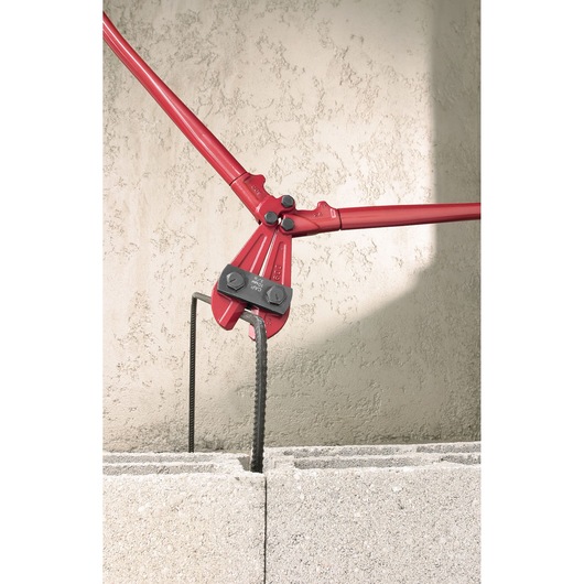 Facom 990_B0 bolt cutter with red handles cutting rebar in concrete blocks, side angle.