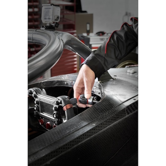 Facom ATCL.S14 ratchet screwdriver used inside a race car cockpit, hand holding tool near steering wheel.