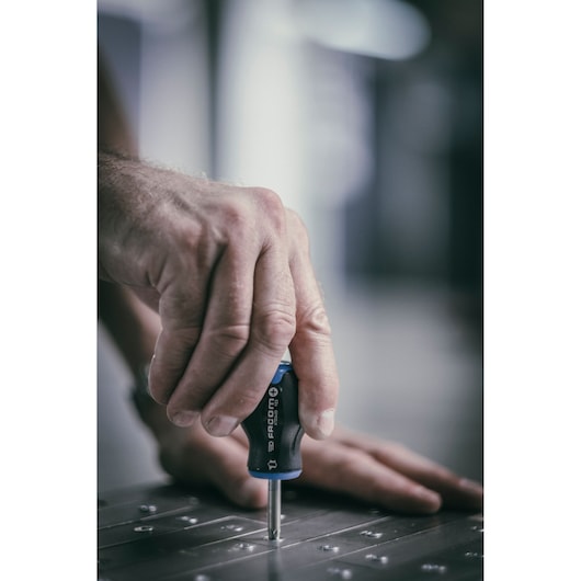 Photo of Facom ATD2X35 screwdriver in use on metal surface, close-up of hand gripping the handle.