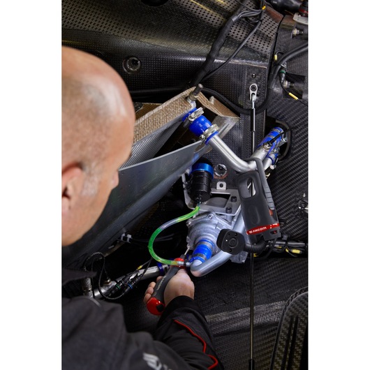 Facom ATPA4V_J23PB cordless ratchet in use tightening blue hoses on a mechanical assembly, close-up angle.