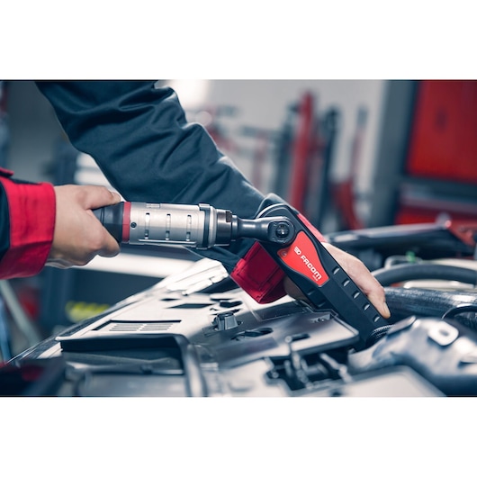 Facom AXS.LPB cordless ratchet wrench in use on an engine, red and black handle, workshop setting.