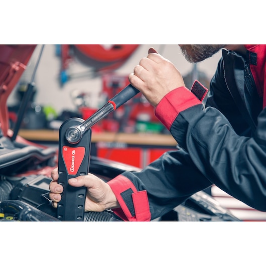 Facom AXS_M torque wrench used by a mechanic in red and black uniform working on a car engine.