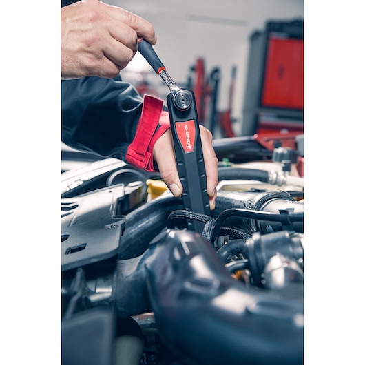 Facom AXS_M ratchet wrench in use on an engine, close-up photography of tool and hands.