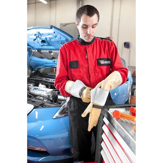 Photo of Facom BC_110VSE protective gloves worn by a mechanic in a red coverall, standing by a blue car in a garage.