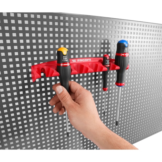 Facom CKS_08 screwdriver rack with three screwdrivers on perforated wall, hand holding one tool, front angle.