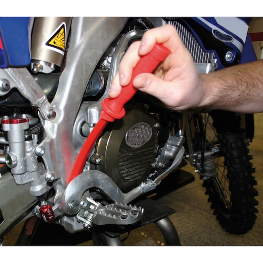 Facom CR.D4PB red plastic lever tool used on motorcycle frame near engine, close-up action.