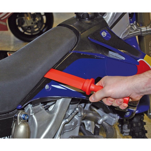 Facom CR.D4PB red plastic tool in hand used on motorcycle seat, side view.