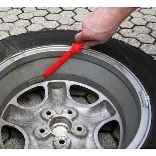 Photo of Facom CR.D4PB red tire lever tool held by hand, removing tire from wheel rim on pavement.