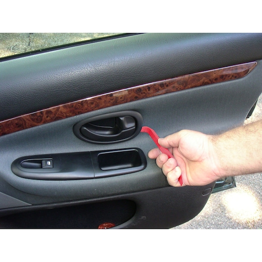 Facom CR.D5PB red trim removal tool used to detach a car door panel, close-up view.