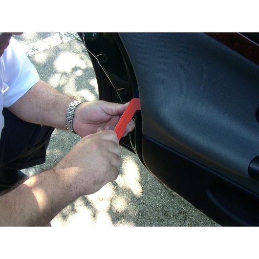 Facom CR.D5PB red trim removal tool in use on a car door panel, close-up photography.