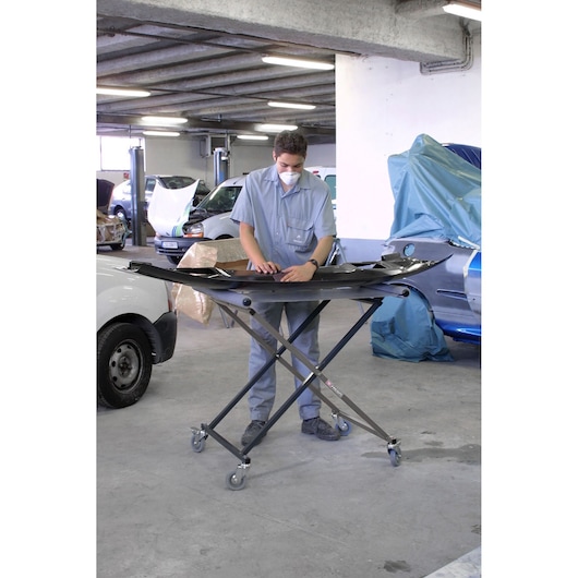 Facom CR_S7 adjustable folding work stand with wheels in a workshop, holding a car part.
