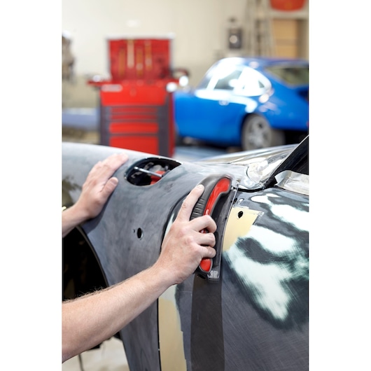 Facom CR_SBS hand sander used on a car body in a workshop, red and black tool, automotive repair context.