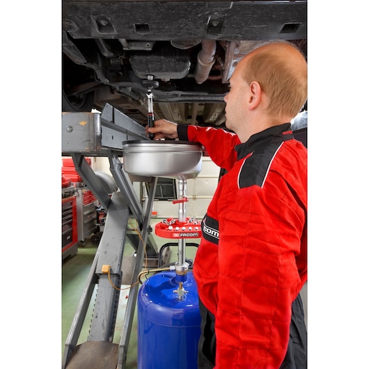 Facom D.48-KITPB oil drain kit in use during automotive maintenance, worker in red uniform operating tool.