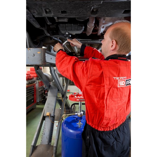Photo of a mechanic in a red Facom jumpsuit using tools under a raised vehicle in a workshop, D_48-KIT.