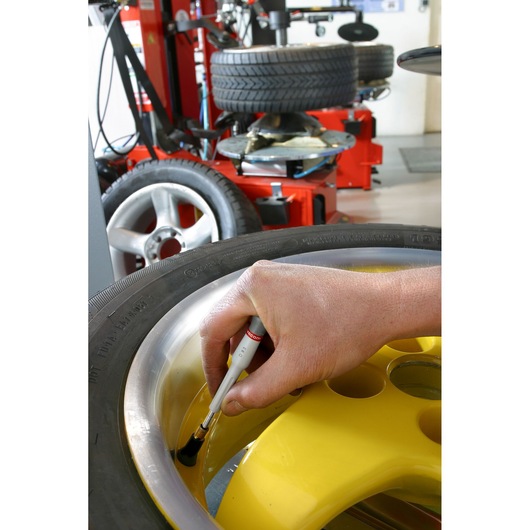 Facom D93 brush applying lubricant to yellow wheel rim, tire changer in background, close-up photography.