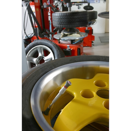 Facom D93 screwdriver on yellow alloy wheel in workshop, tire changing equipment in background.