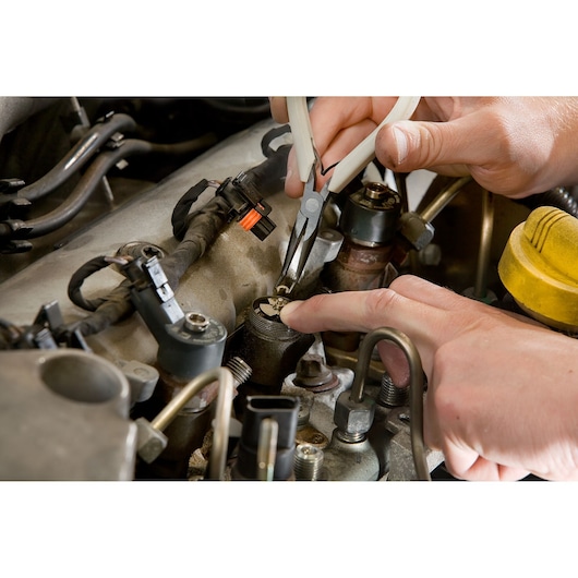 Facom DCRIP pliers used for engine repairs, close-up of hands working in automotive engine bay.