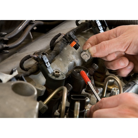 Facom DCRIP tool used on engine component, close-up view showing hands in automotive maintenance setting.