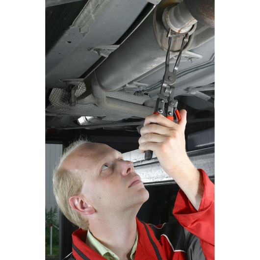 Facom exhaust pipe pliers DE.CPB in use removing an exhaust clamp under a car.