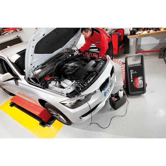 Facom DF_101 automotive diagnostic machine connected to a white car in a workshop with technician working on the engine.