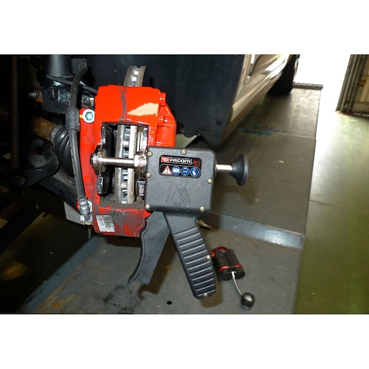 Facom DF_23 brake caliper tool in use on red car brake assembly, with handle and adjustment knob visible.