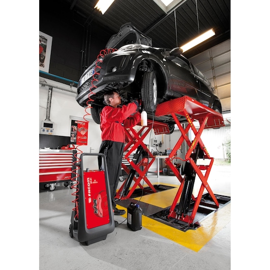Facom DF_81 automotive tool in workshop with technician near black car on red lift, front angle.