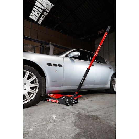 Facom DL_2LP low-profile floor jack with red handle lifting a silver car in a garage, side angle view.