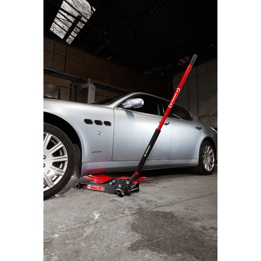 Facom DL_2LP low profile hydraulic floor jack in red and black lifting a silver car in a garage, side view.