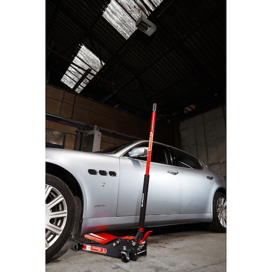 Facom DL_2LP red and black low-profile hydraulic floor jack positioned under a silver car in a garage.