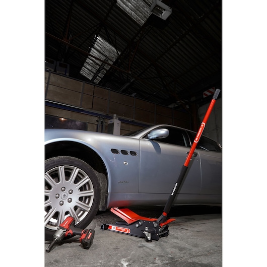 Facom DL_2LP car jack with red handle positioned under a silver car, garage setting, side view.