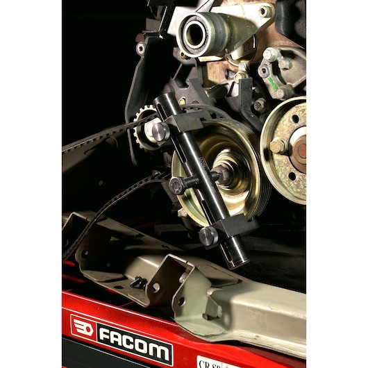 Facom DM_50 automotive pulley holder tool mounted on engine assembly, side angle.