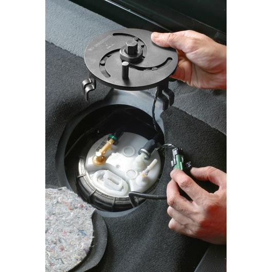 Facom DMJL fuel pump tool being used to remove a fuel tank lock ring in a car interior.