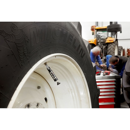 Facom DRSIL tire pressure gauge on tractor wheel in workshop with tool chest and two people working.