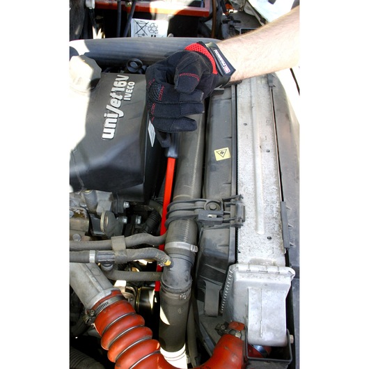 Facom DT_TWA glove gripping a red-handled tool while working on a car engine bay, close-up view.