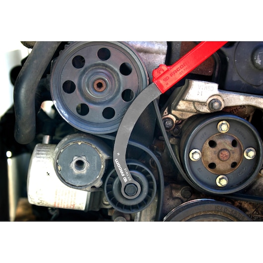 Facom DT_TWA automotive belt tool with red and black handle positioned on engine pulley, close-up view.