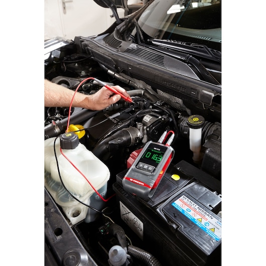 Photo of Facom DX.V12PB automotive digital multimeter testing a car engine, close-up view of device in use.