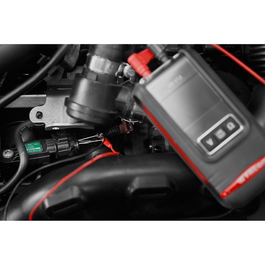 Facom DX.V12PB automotive diagnostic tool with red leads connected to a car engine, close-up view.